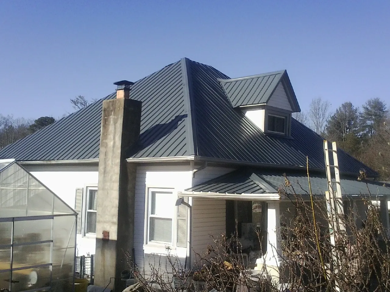 Dark blue standing seam metal roof on a white farmhouse with dormer — Slate & Tile Roof Repair by Roofing Brothers in Lake Forest