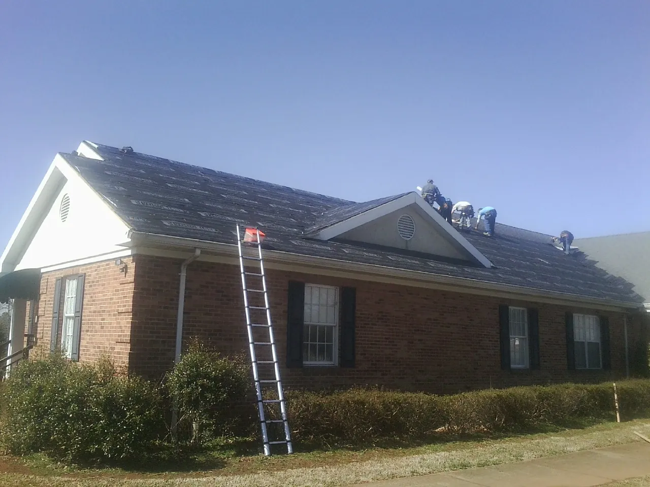 Crew tearing shingles off a brick ranch roof with a ladder set — Metal Roof Repair work by our crew in Lake Forest