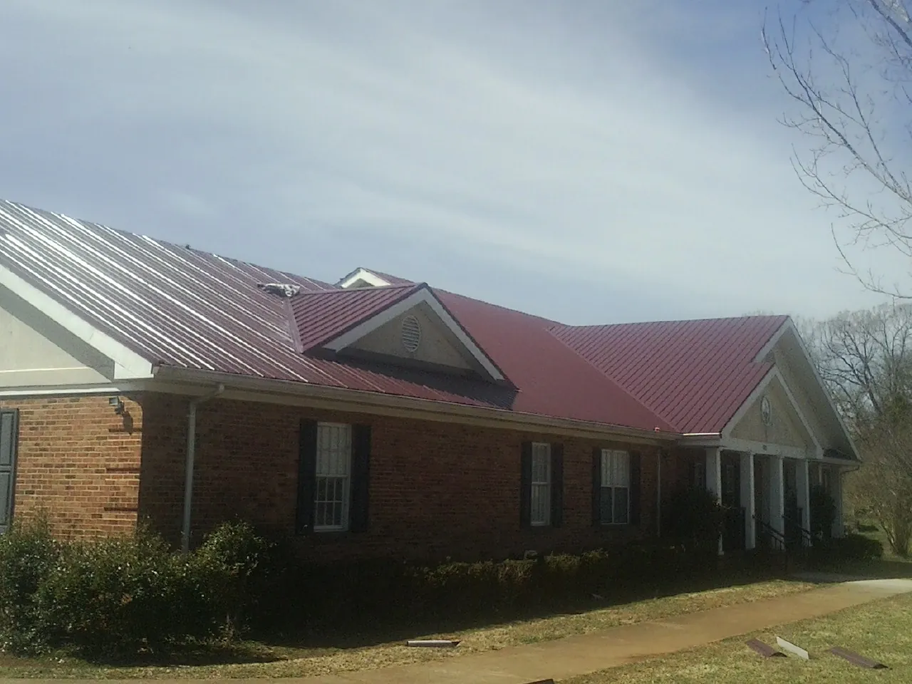 Red metal roof with gabled entries on a long brick building, from a Hail Damage Roof Repair job in Lake Forest