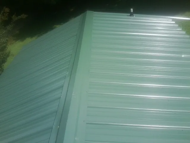 New green metal panels meeting at the ridge of a roof — Flat Roof Repair work by our crew in Lake Forest