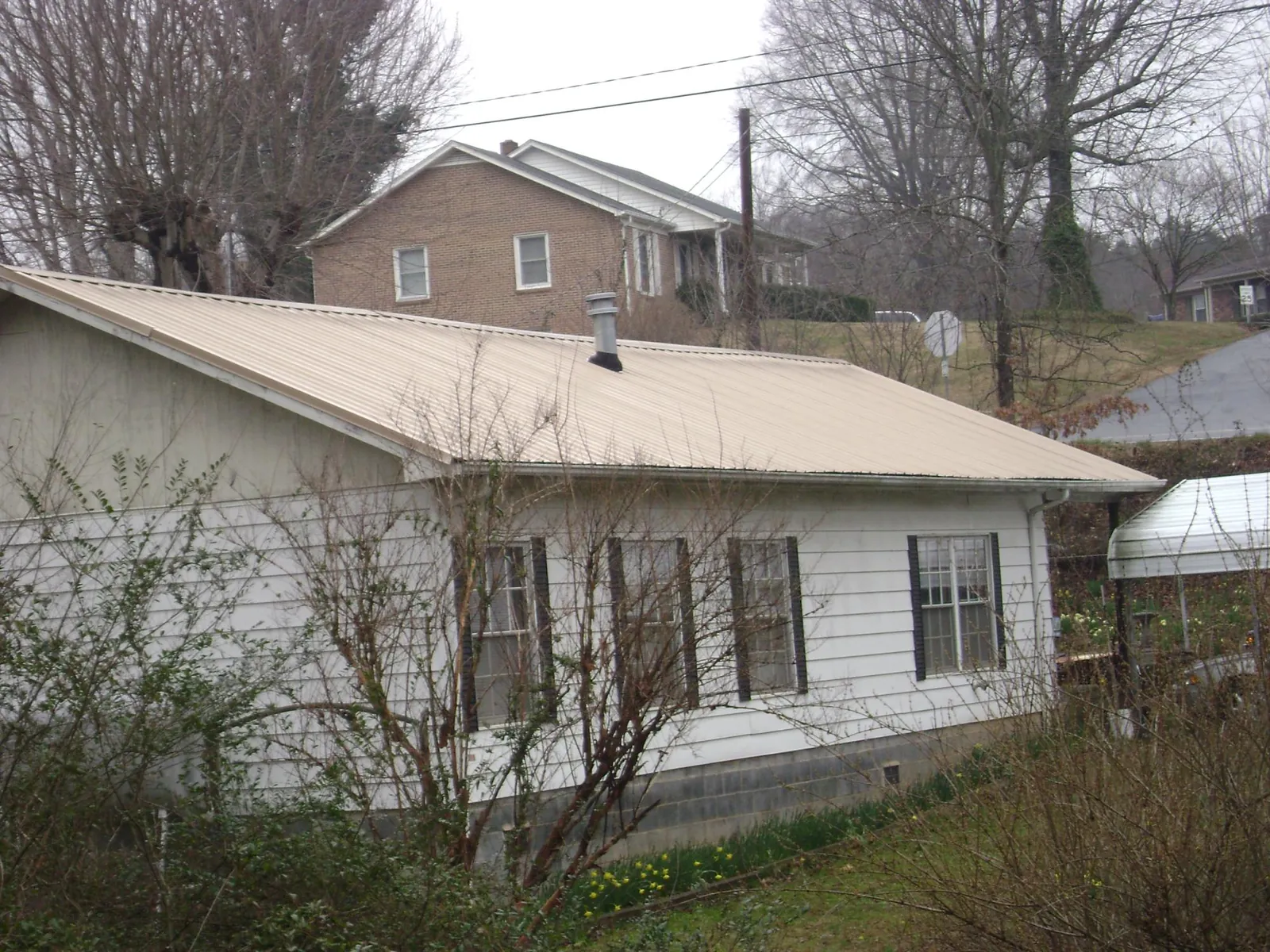 Tan metal roof on a white sided house set into a hillside — Commercial Roofing by Roofing Brothers in Lake Forest