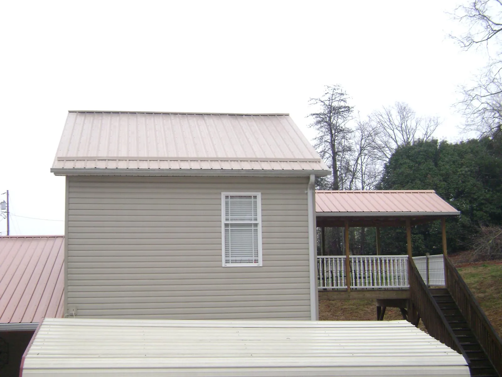Tan metal roofs on a two story addition and attached porch, from a Roof Replacement job in Lake Forest